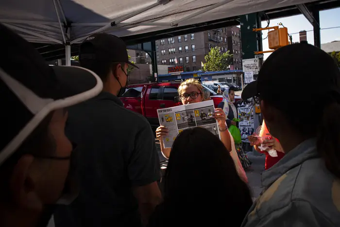 A person addressing a large gathered group on the sidewalk holds a pamphlet titled, "Know Your Rights."